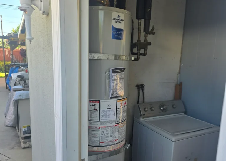 A water heater installation and washing machine are placed side by side in a small utility area with a partially open door, next to an outdoor space.