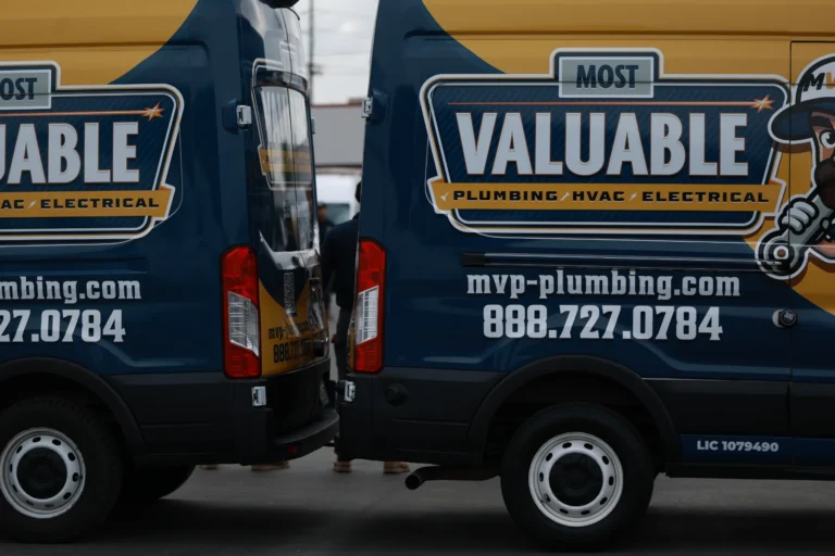 Two MVP Plumbing vans with their back bumpers nearly touching, displaying company branding, contact information, and tankless water heater installation services on the sides.