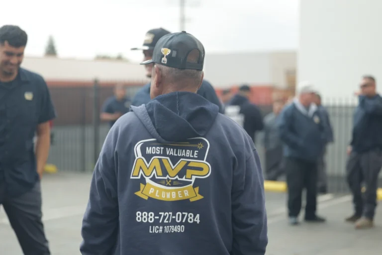 A person wearing a hoodie and cap with "MVP Plumber" and contact information stands outside among a group of people, ready to assist with trenchless sewer line repair services.