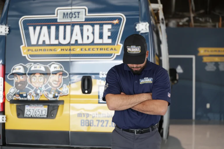 A man in a "Most Valuable" uniform stands with arms crossed in front of a van advertising plumbing, HVAC, electrical services, and water softener repair.