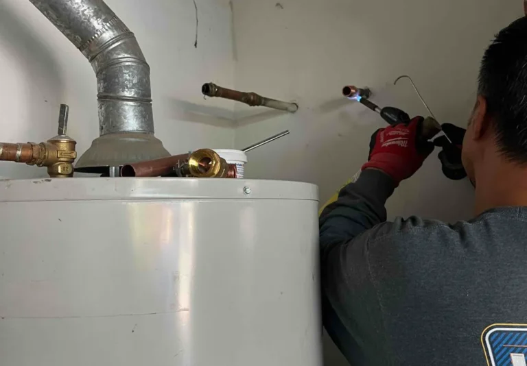 A plumber uses a torch to solder copper pipes during a water heater repair in a utility room.