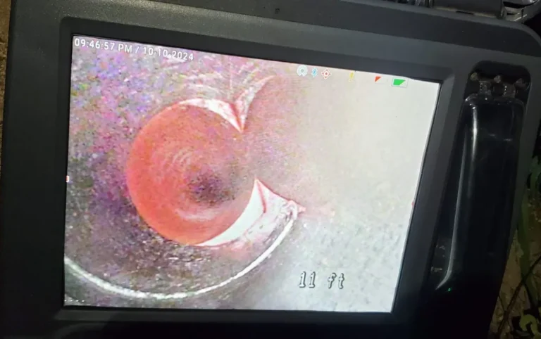 Close-up of a monitor displaying a live camera inspection service inside a pipe, revealing a circular tunnel and measurement reading of 11 ft.