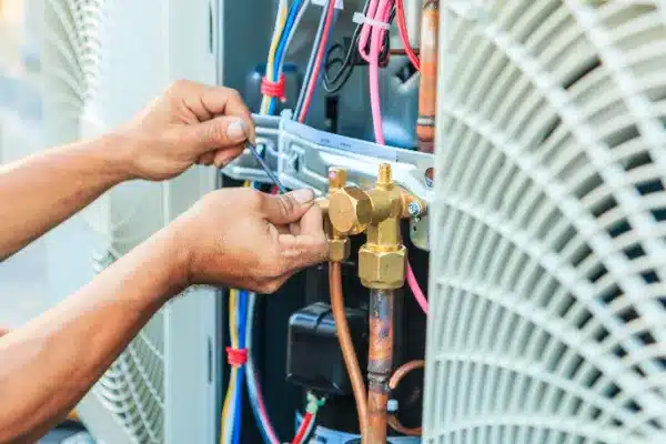 Person working with tools on an HVAC unit, adjusting copper pipes and wires.