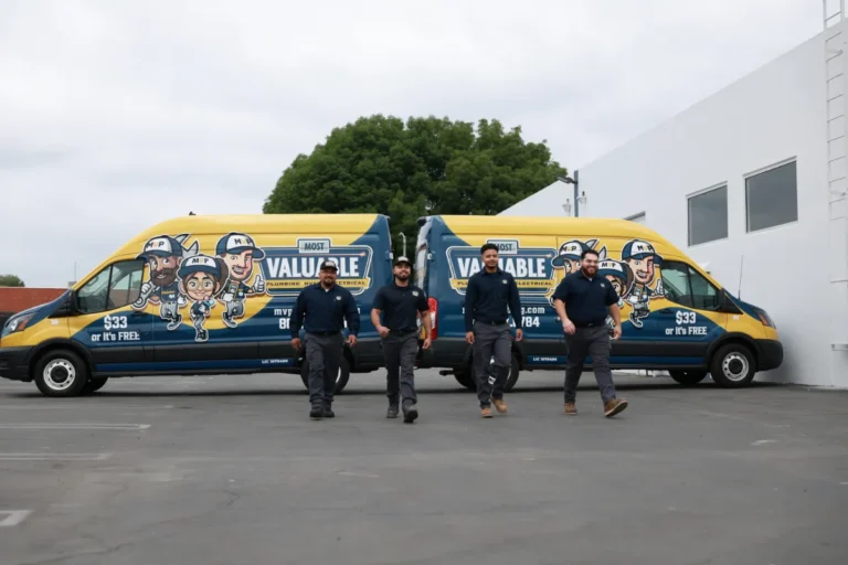 Four workers in navy uniforms walk in front of two yellow and blue vans parked side by side, both displaying "Most Valuable" branding and cartoon graphics.