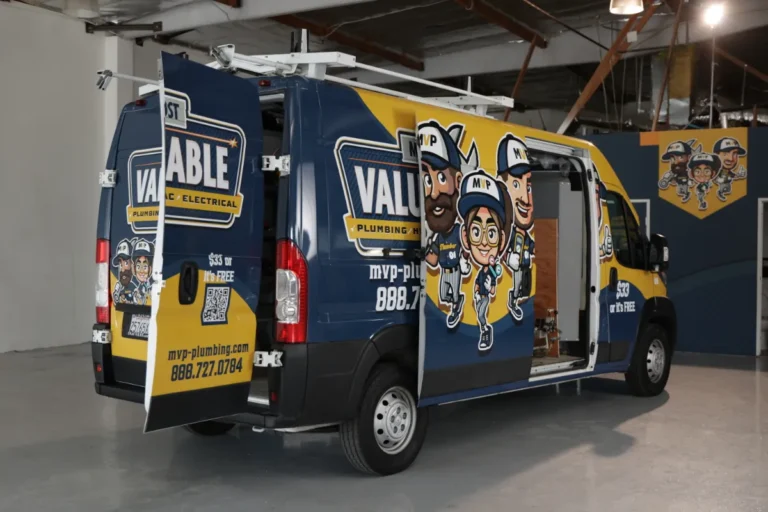 A blue and yellow van with "Valuable Plumbing & Electrical" branding and cartoon characters parked inside a warehouse with its side and rear doors open.