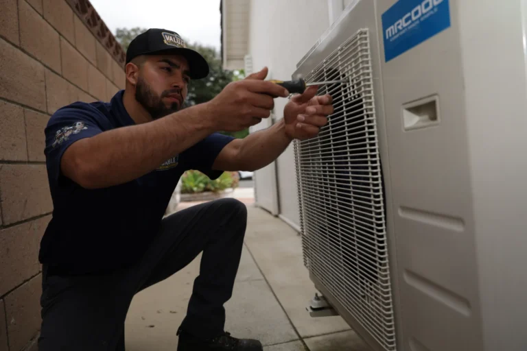 A technician in uniform uses a screwdriver to service an outdoor air conditioning unit labeled “MRCOOL” next to a house.