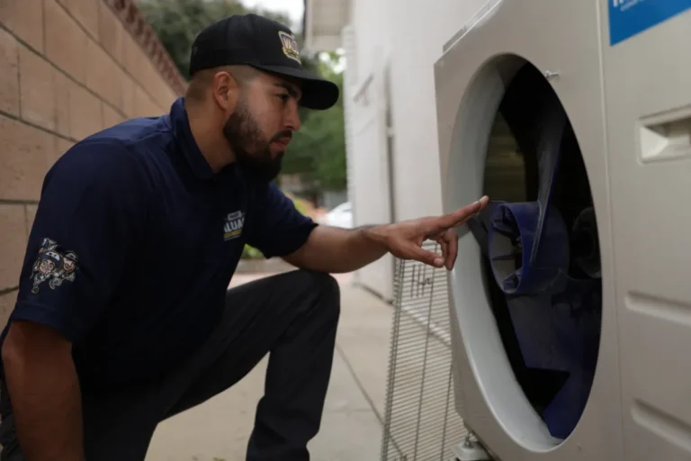 A man in a uniform inspects the interior of a white washing machine outdoors, closely examining the drum with his finger.