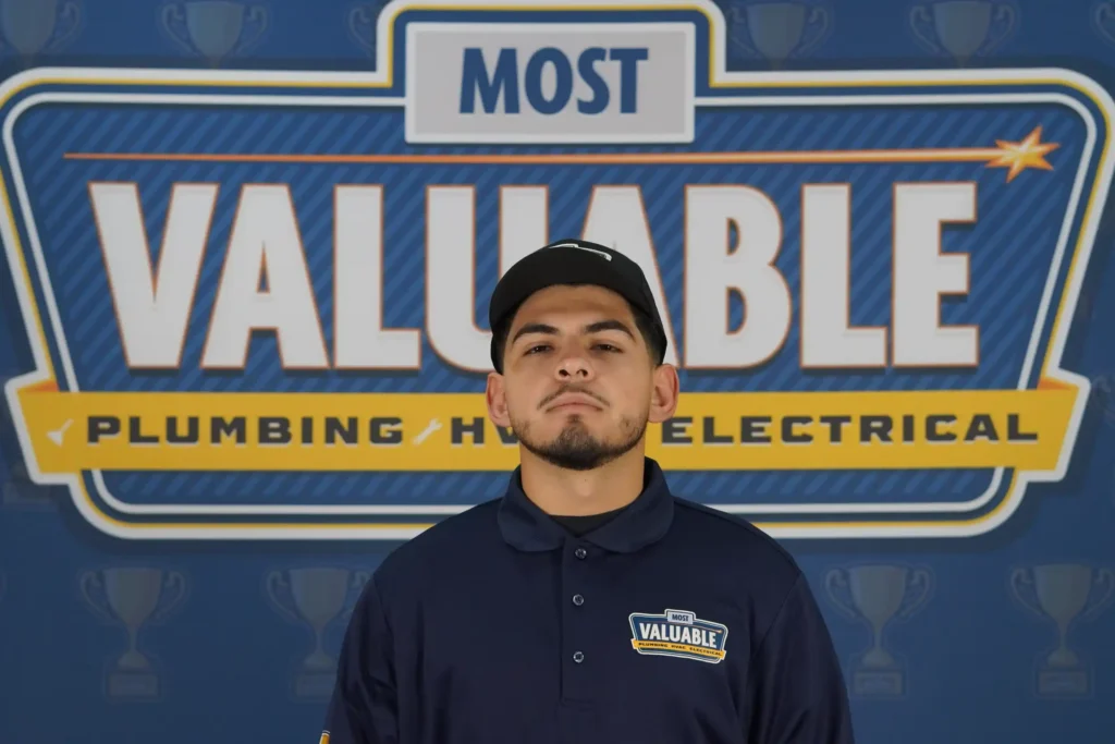 A man wearing a "Most Valuable" uniform stands in front of a backdrop that reads "Most Valuable Plumbing HVAC Electrical," ready to meet the team and showcase their top-notch services.