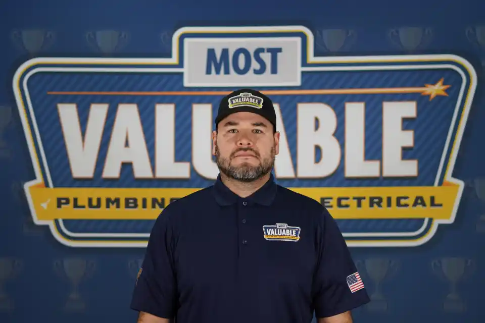 Meet the team: A man in a "Most Valuable" uniform and cap stands in front of a sign reading "Most Valuable Plumbing & Electrical.
