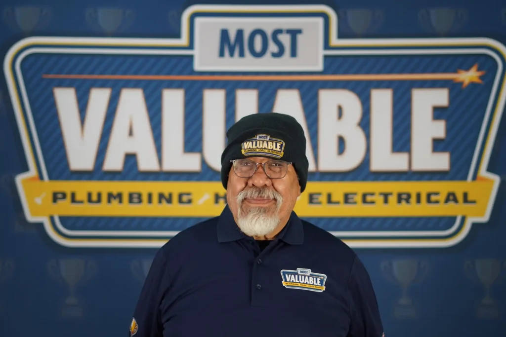 Meet the team: An older man wearing glasses, a beanie, and a shirt with "Most Valuable" logos stands in front of a backdrop reading "Most Valuable Plumbing HVAC Electrical.