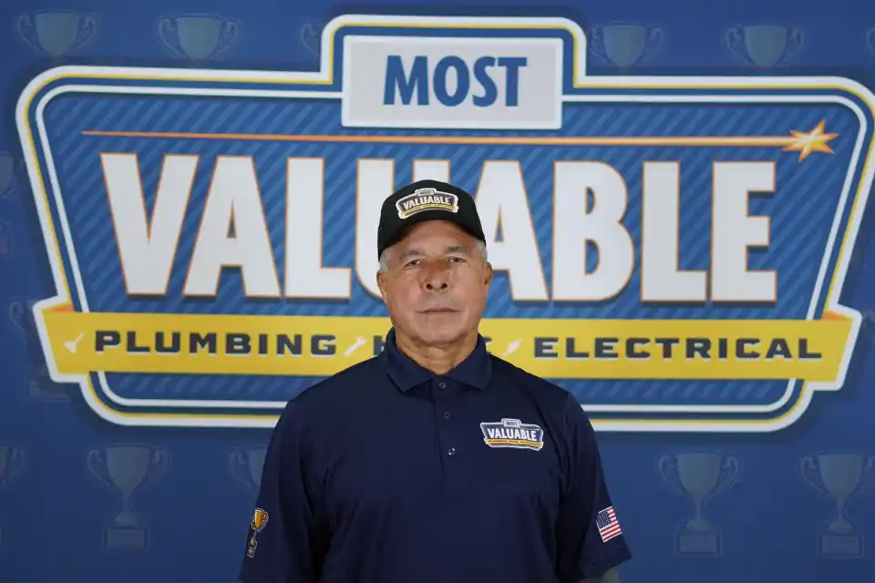 Meet the team: A man in a dark polo shirt and hat stands in front of a sign that reads "Most Valuable Plumbing & Electrical.