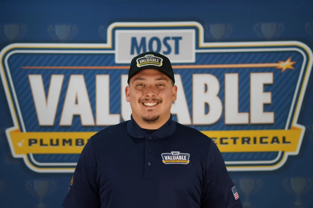 Meet the team: A man in a dark polo and cap with "Valuable" logos stands smiling in front of a backdrop reading "Most Valuable Plumbing & Electrical.