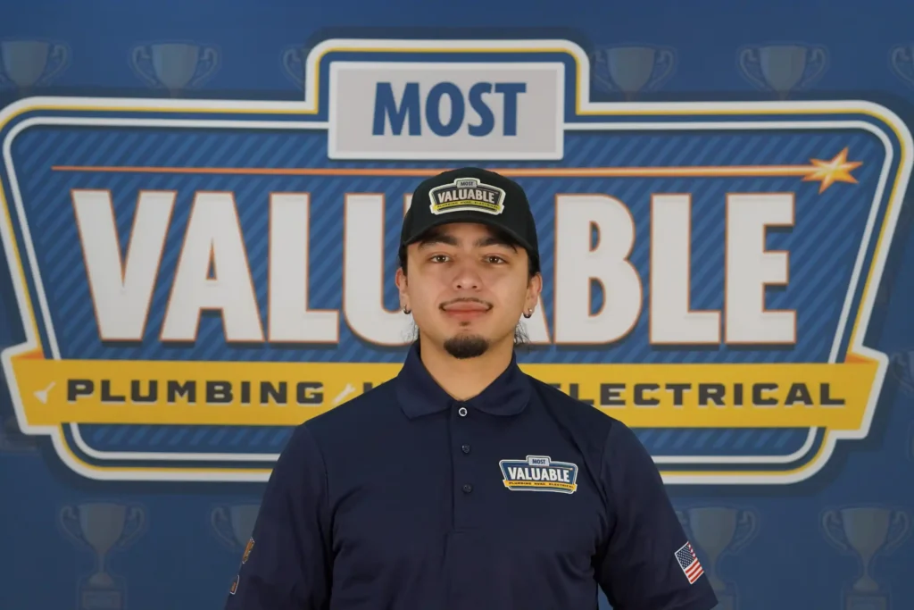 A person wearing a "Most Valuable" hat and shirt stands in front of a backdrop that reads "Most Valuable Plumbing and Electrical," ready to meet the team.