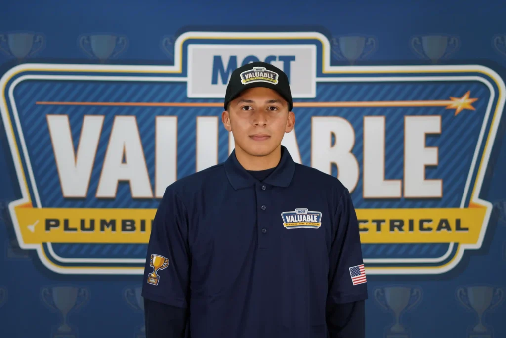 Meet the team: A man in a "Most Valuable" uniform and hat stands in front of a sign reading "Most Valuable Plumbing Electrical.