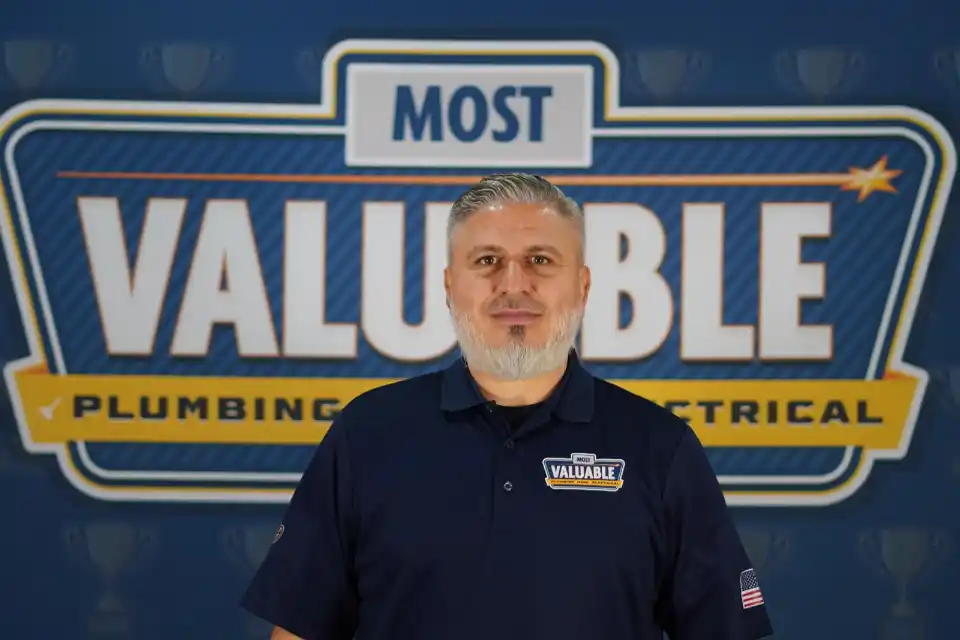 Meet the team: A man stands in front of a sign that reads "Most Valuable Plumbing Electrical," wearing a navy shirt with the "Most Valuable" logo.