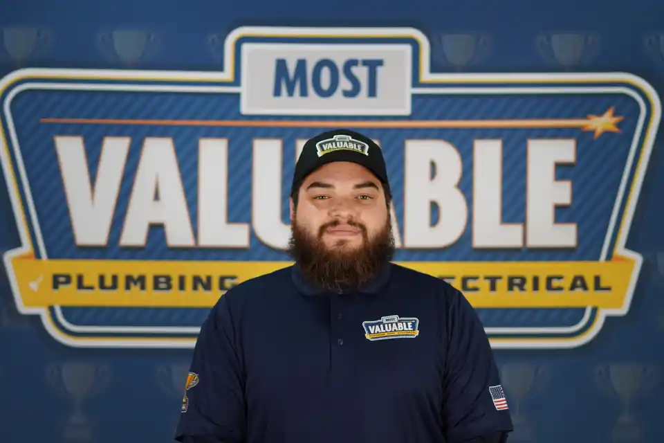 Meet the team: A man with a beard, wearing a "Most Valuable" cap and shirt, stands in front of a sign that reads "Most Valuable Plumbing & Electrical.