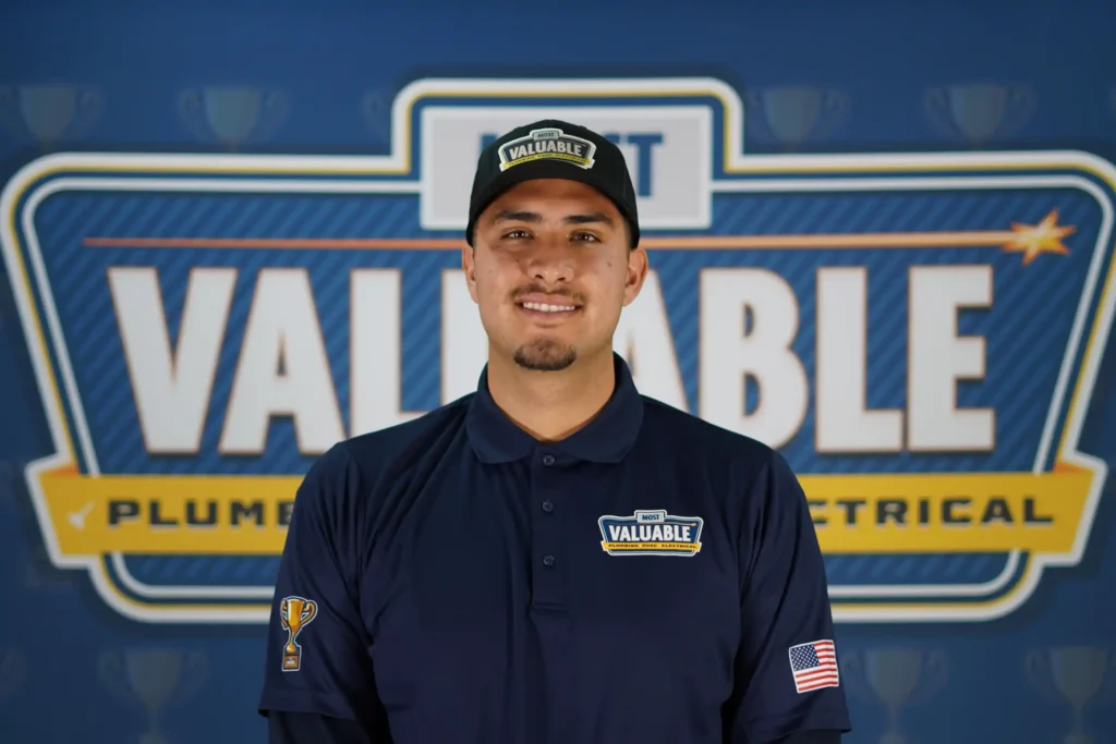 Meet the team: A man wearing a navy uniform and hat with "Valuable" logos stands in front of a "Valuable Plumbing Electrical" sign on a blue background.