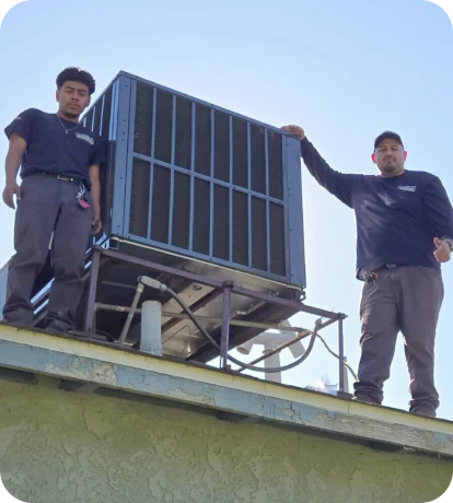 Two workers in uniforms stand on a roof next to a large air conditioning unit, with one resting his hand on the unit and the other standing to the side.