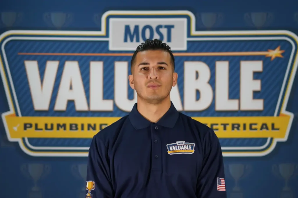 Meet the team: A man in a navy uniform stands in front of a sign that reads "Most Valuable Plumbing Electrical.
