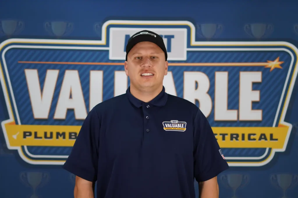 Meet the team: A man in a navy shirt and cap with "Most Valuable" logos stands in front of a "Most Valuable Plumbing & Electrical" sign.