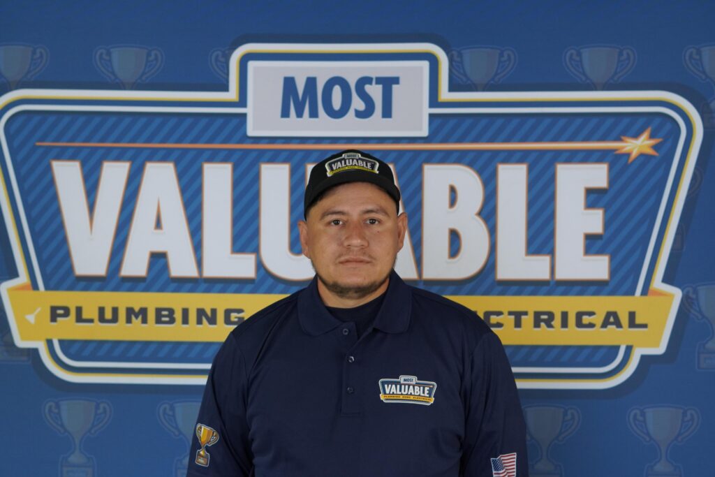 Meet the team: A man in a navy blue "Most Valuable" uniform stands proudly in front of a backdrop featuring the "Most Valuable Plumbing & Electrical" signage.