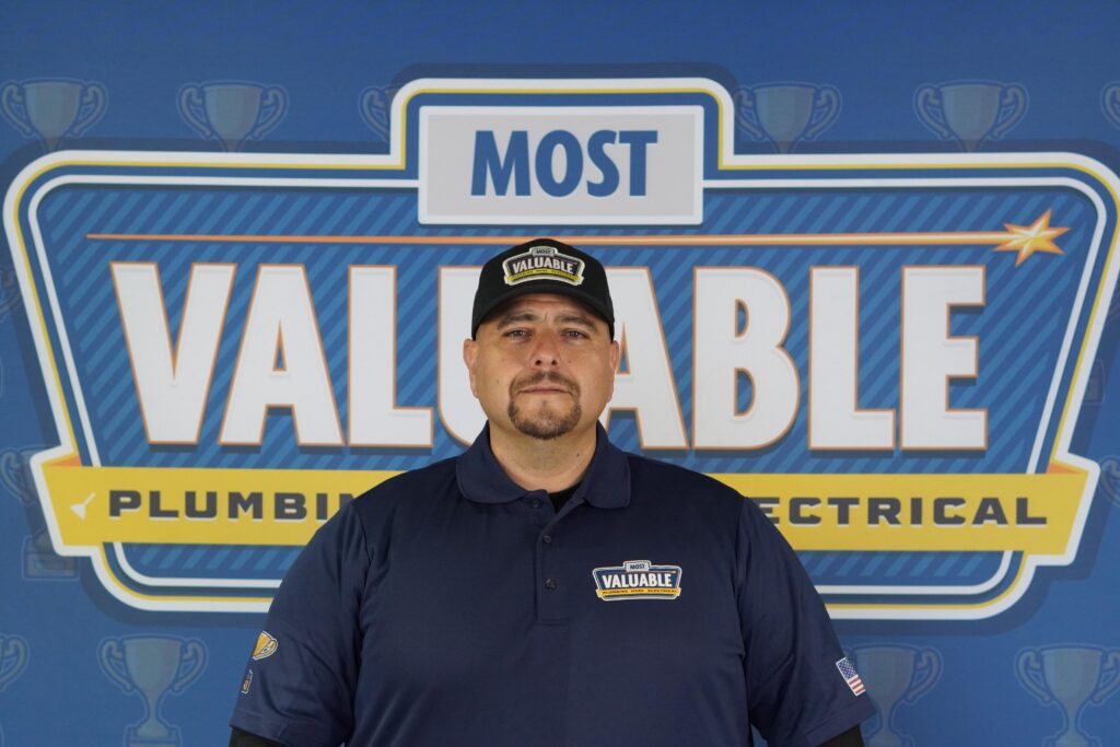 Meet the team: A man wearing a "Most Valuable" cap and shirt stands in front of a backdrop that reads "Most Valuable Plumbing & Electrical.